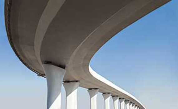 Low-angle view of a curved concrete overpass with white pillars set against a clear blue sky.