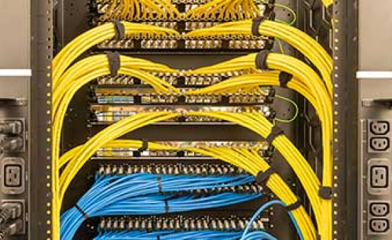 Thick yellow cables are neatly bundled and arch over blue cable bundles inside a server rack.