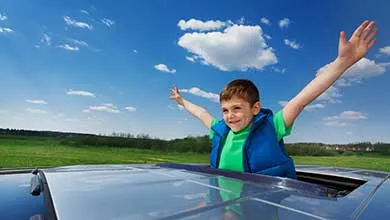 Portrait of happy smiling five years old boy enjoying freedom on the sunroof of a car