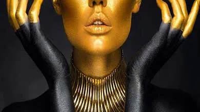 Close-up of a person with metallic gold face paint, a matching ribbed necklace, and black-and-gold painted hands framing their face.