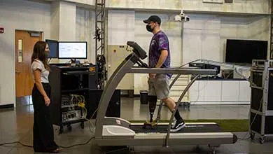 A man with two prosthetic legs walks on a treadmill in a research lab as a woman monitors him.