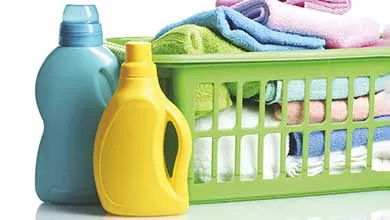 A blue and a yellow laundry detergent bottle beside a green basket filled with folded, colorful towels.