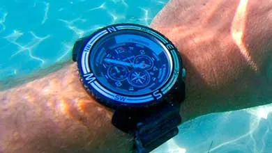 A large black dive watch on a person's wrist, underwater in clear turquoise water.