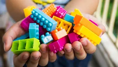 Hands holding a collection of brightly colored plastic building blocks in various shapes and sizes.