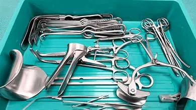 Stainless steel surgical instruments, including forceps, retractors, and speculums, arranged in a teal tray.
