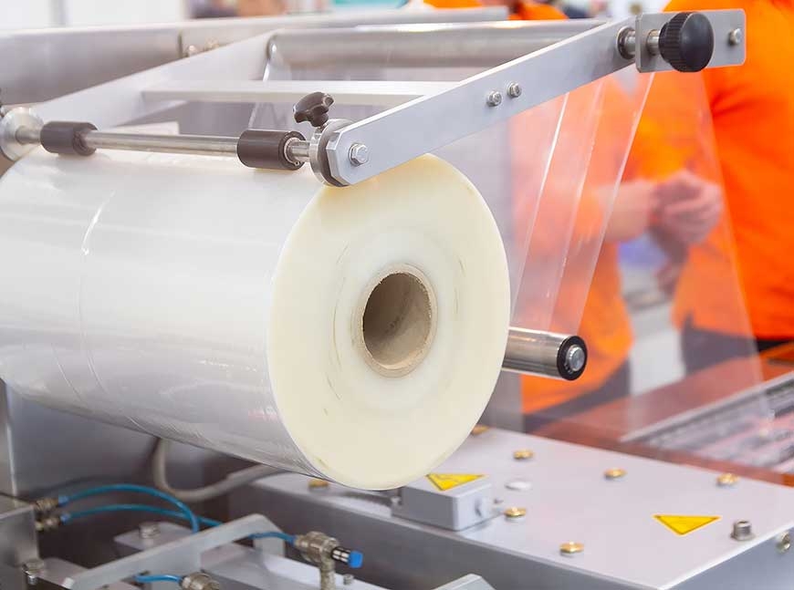 A machine with a large roll of plastic packaging film in a factory